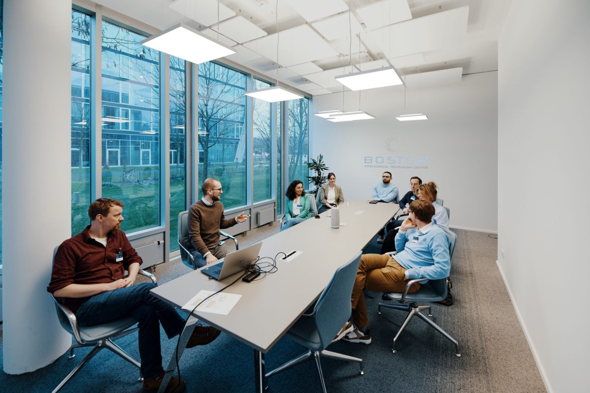 Auf dem Bild sind mehrere Personen in einem Konferenzraum zu sehen, die an einem Workshop teilnehmen. Der Raum ist gut beleuchtet und mit Stühlen und einem Konferenztisch ausgestattet. Die Teilnehmer sitzen aufrecht an ihren Plätzen und hören konzentriert einem Moderator zu, der am Tisch sitzt und etwas erklärt. Die Szene vermittelt ein Gefühl von Interaktion und Wissensaustausch in einer professionellen Umgebung.